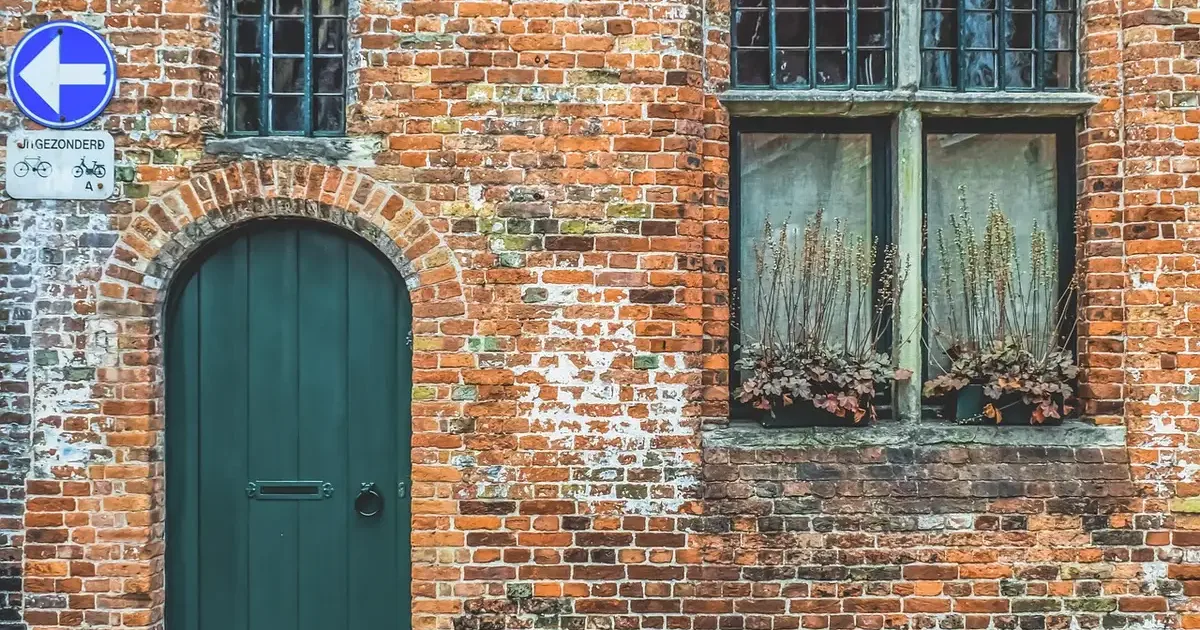 Old brick house front with an arched green door and small-paned windows