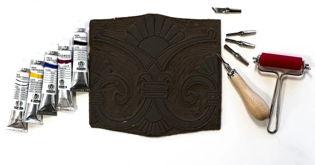 Carved linoleum block beside an ink roller, cutting tools and tubes of ink