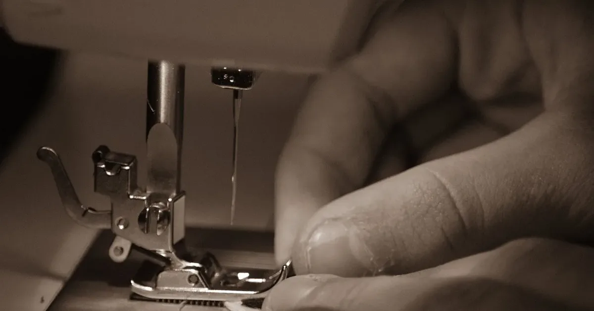 Fingers guiding fabric under a sewing machine needle, in sepia