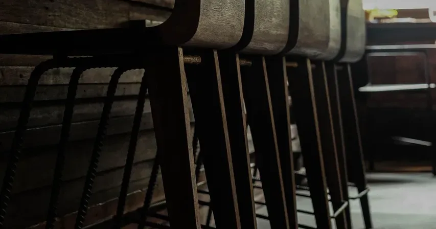 Row of wooden bar stools along a dark counter by a window