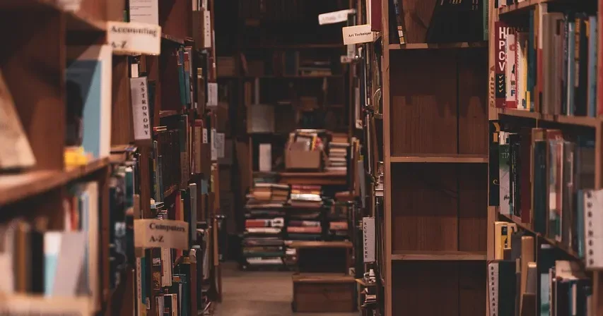 Narrow aisle between tall wooden shelves in a crowded bookshop