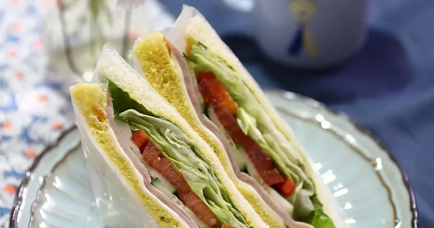 Sandwich halves on a plate beside a cup of tea and a jar of daisies