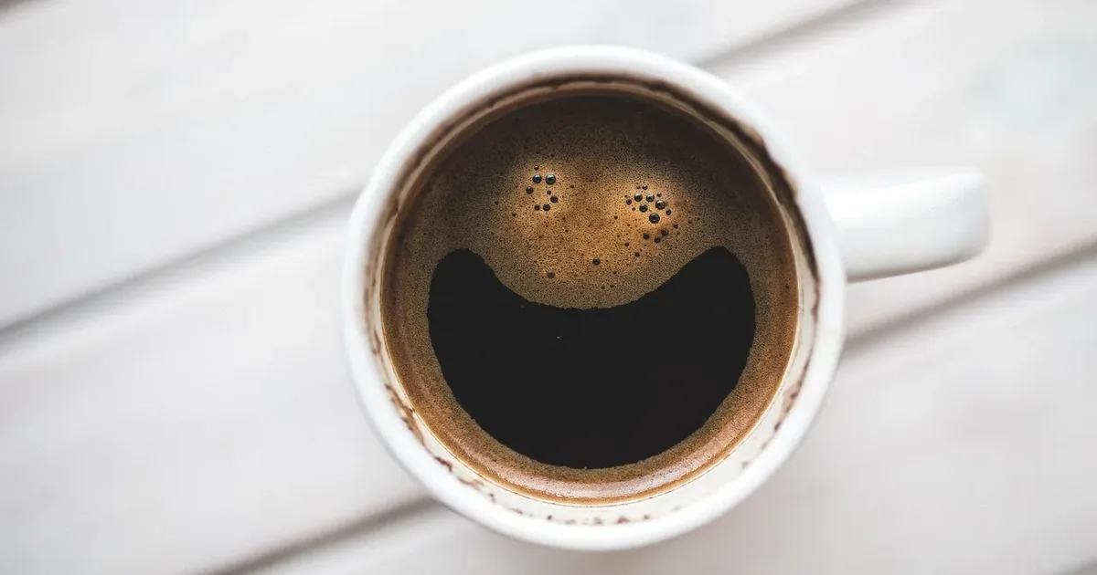 Black coffee in a white cup, the foam shaped like a smile