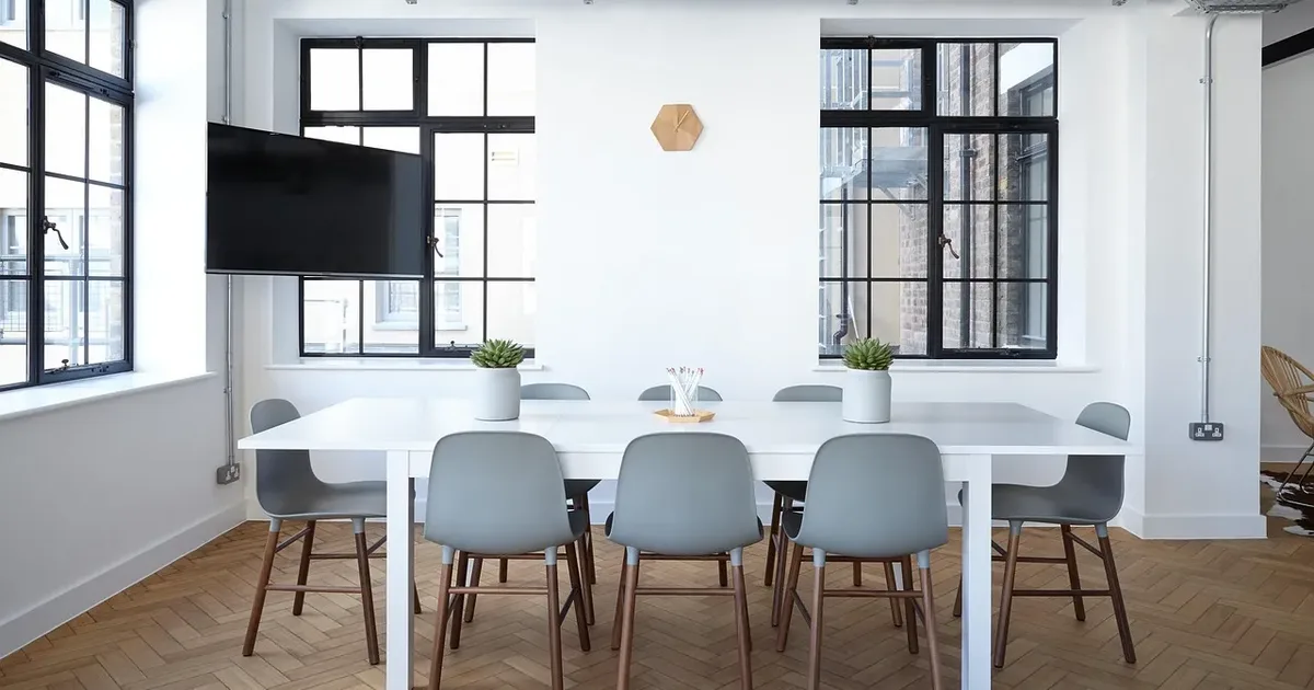 White meeting room with a long table, grey chairs, steel-framed windows and a herringbone floor