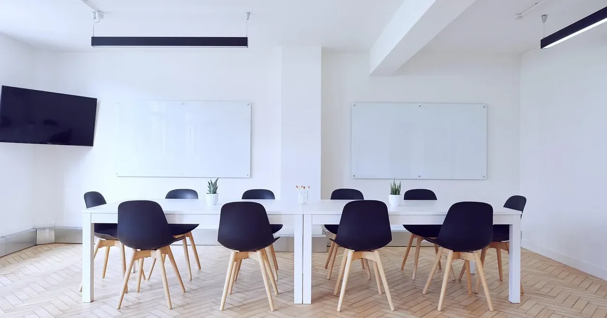 Empty white room with two tables, navy chairs and whiteboards on the walls