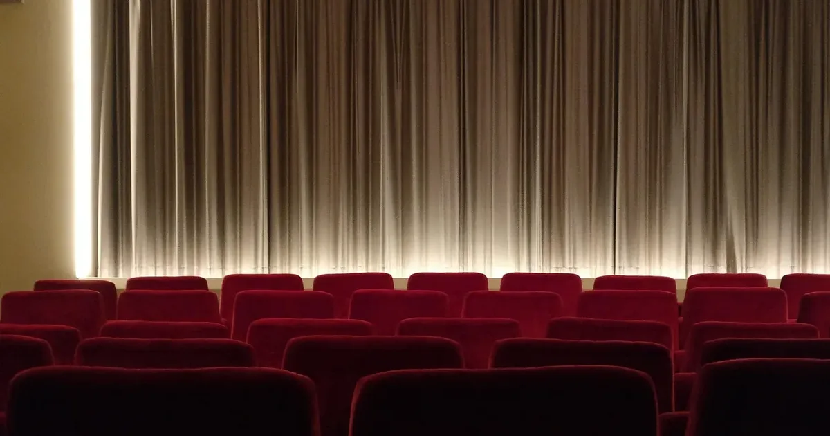 Rows of red velvet cinema seats before a softly lit pleated curtain