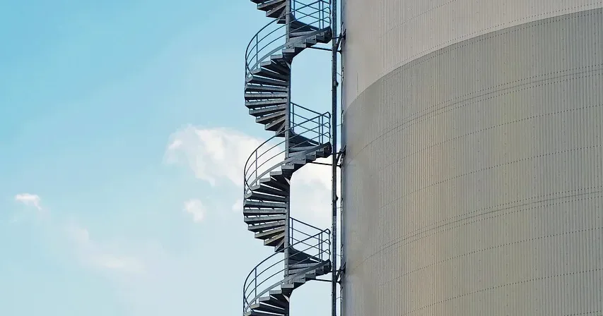 Spiral steel staircase running up the side of a tall pale silo against a blue sky